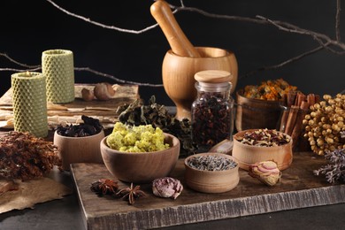Many different dry herbs, flowers and mortar with pestle on dark grey table