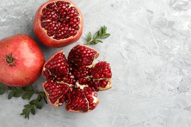 Photo of Fresh pomegranates and green leaves on grey textured table, flat lay. Space for text