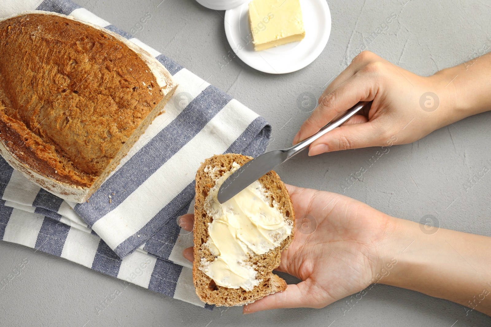 Photo of Woman spreading tasty butter onto bread over grey table, top view