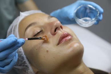 Photo of Cosmetologist applying cosmetic product for chemical peeling on client's face in salon