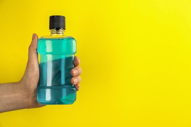 Photo of Woman holding bottle with mouthwash on yellow background, closeup. Space for text