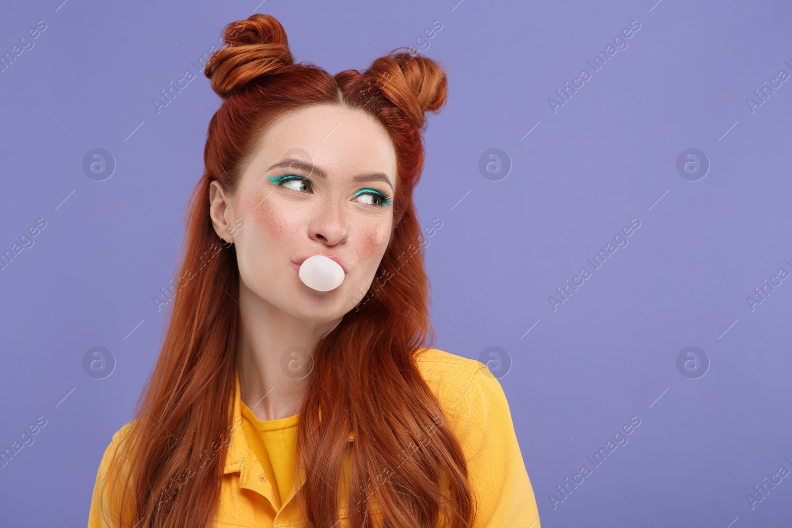 Photo of Beautiful woman with bright makeup blowing bubble gum on violet background. Space for text
