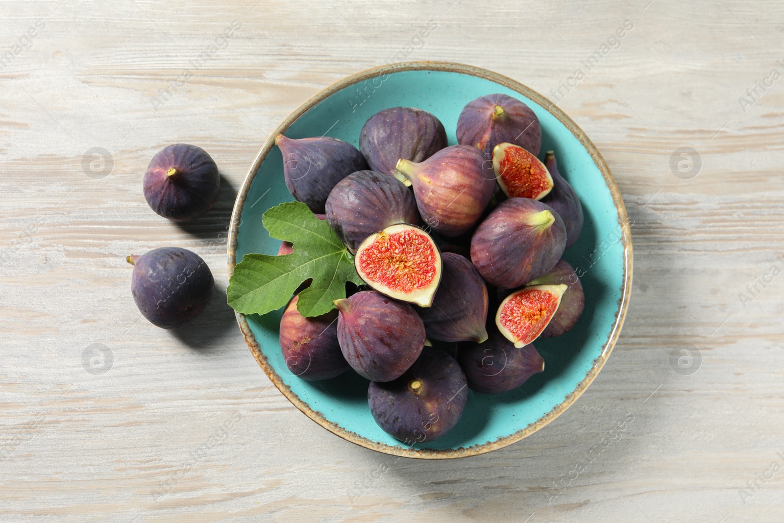 Photo of Plate with fresh ripe figs and green leaf on white wooden table, flat lay