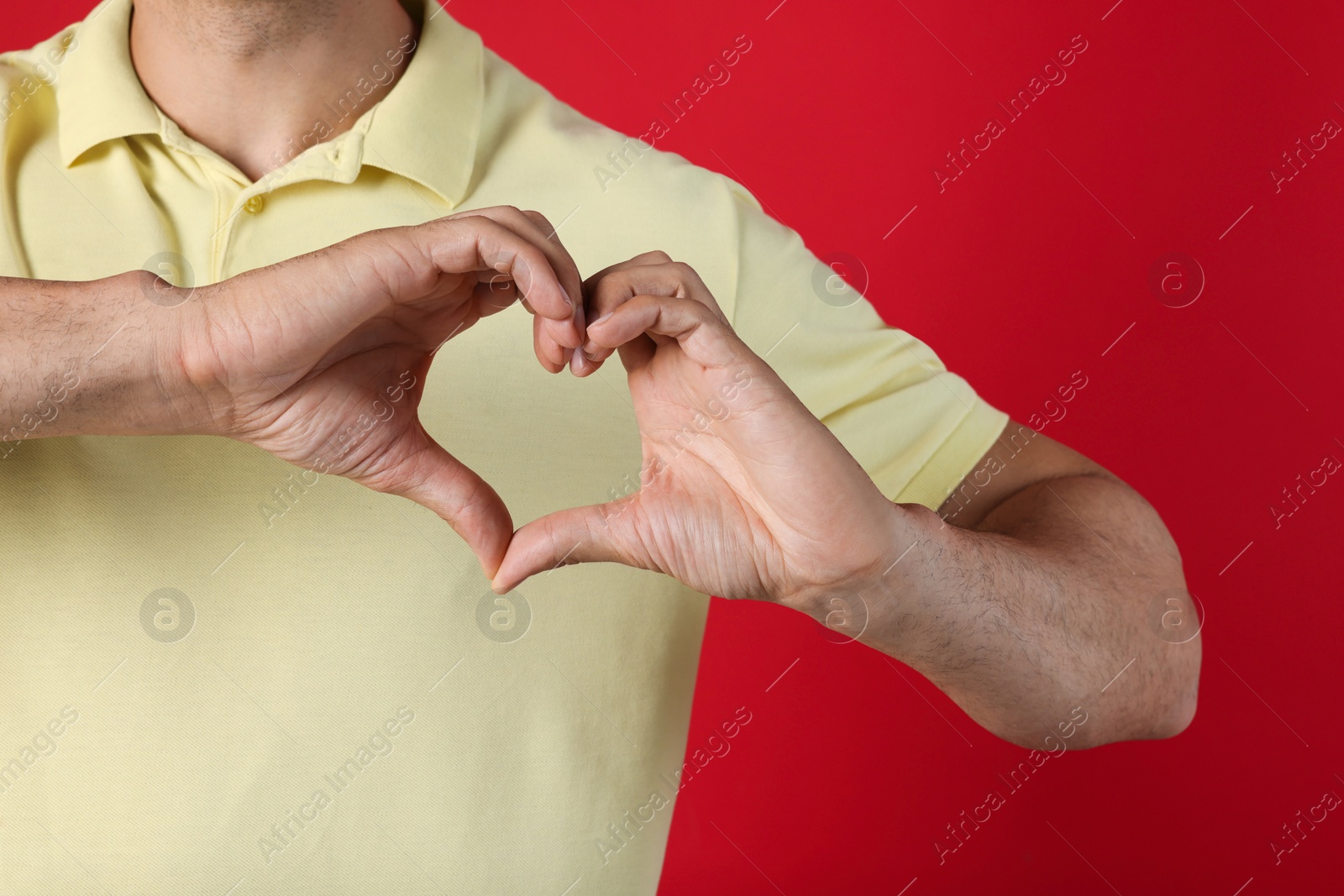 Photo of Man making heart with hands on red background, closeup