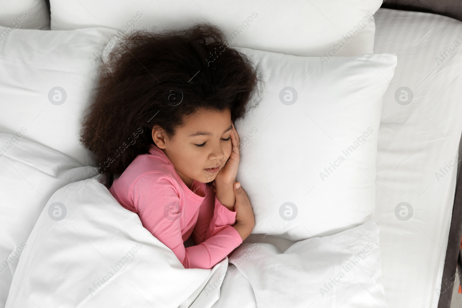 Photo of Cute little African-American girl sleeping in bed, top view