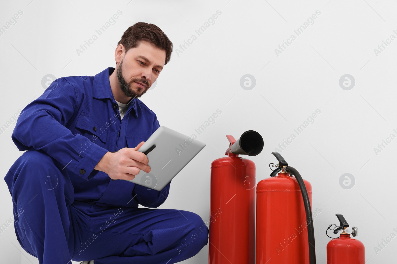 Photo of Man with tablet checking fire extinguishers indoors