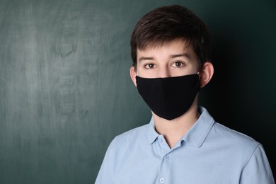 Boy wearing protective mask near chalkboard, space for text. Child safety