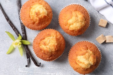 Photo of Delicious sweet muffins, vanilla pods and brown sugar on light grey textured table, flat lay