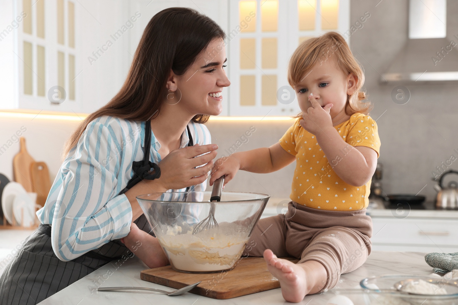 Photo of Mother and her little daughter cooking dough together in kitchen