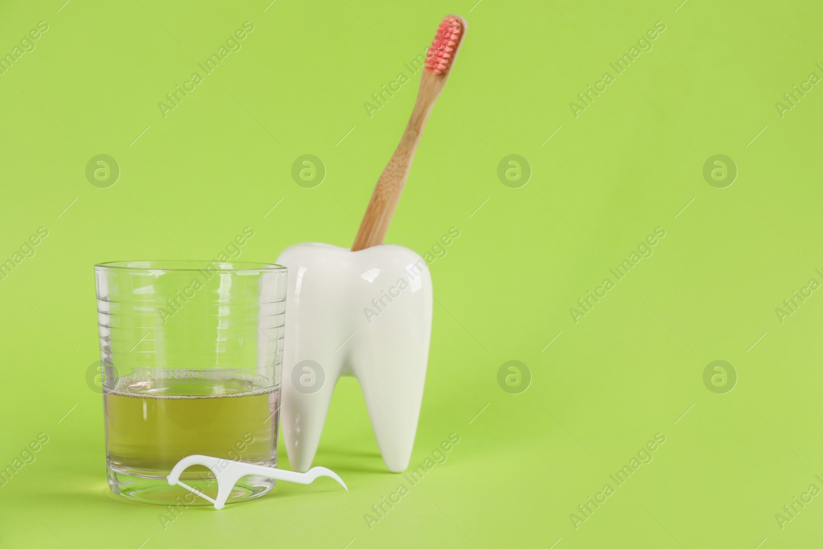 Photo of Mouthwash, toothbrush, holder and dental floss pick on light green background, space for text