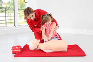 Photo of Instructor with little girl practicing first aid on mannequin indoors