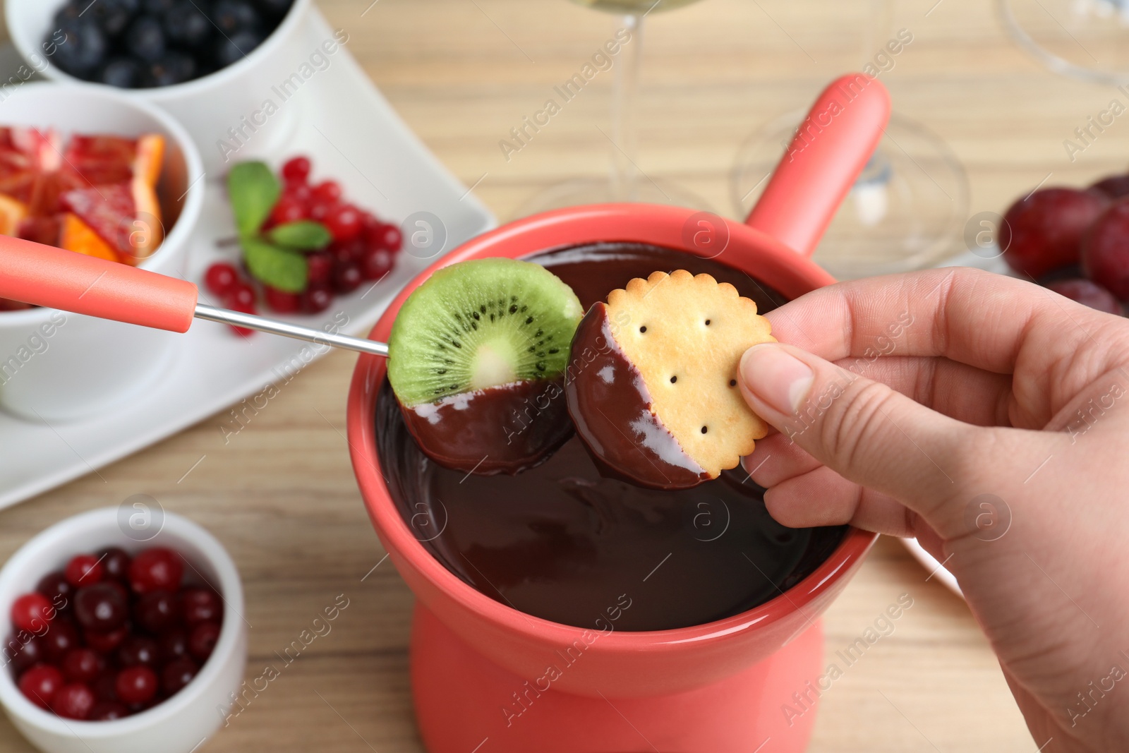 Photo of Woman dipping cookie and kiwi slice into pot with chocolate fondue at table, closeup