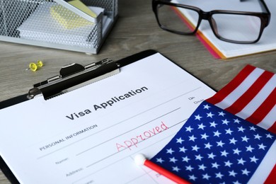 Visa application form with word Approved and American flag on wooden table, closeup