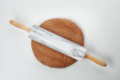 Raw rye dough and rolling pin on white background, top view