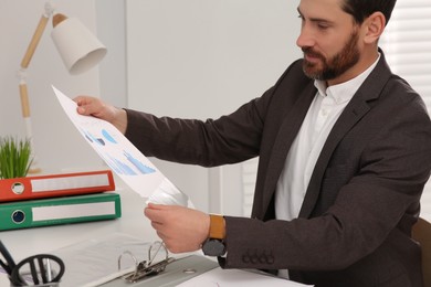 Businessman putting document into punched pocket at white table in office
