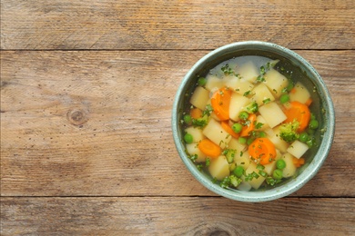 Photo of Bowl of fresh homemade vegetable soup on wooden background, top view. Space for text