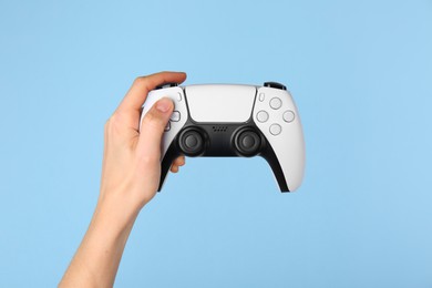 Woman with game controller on light blue background, closeup