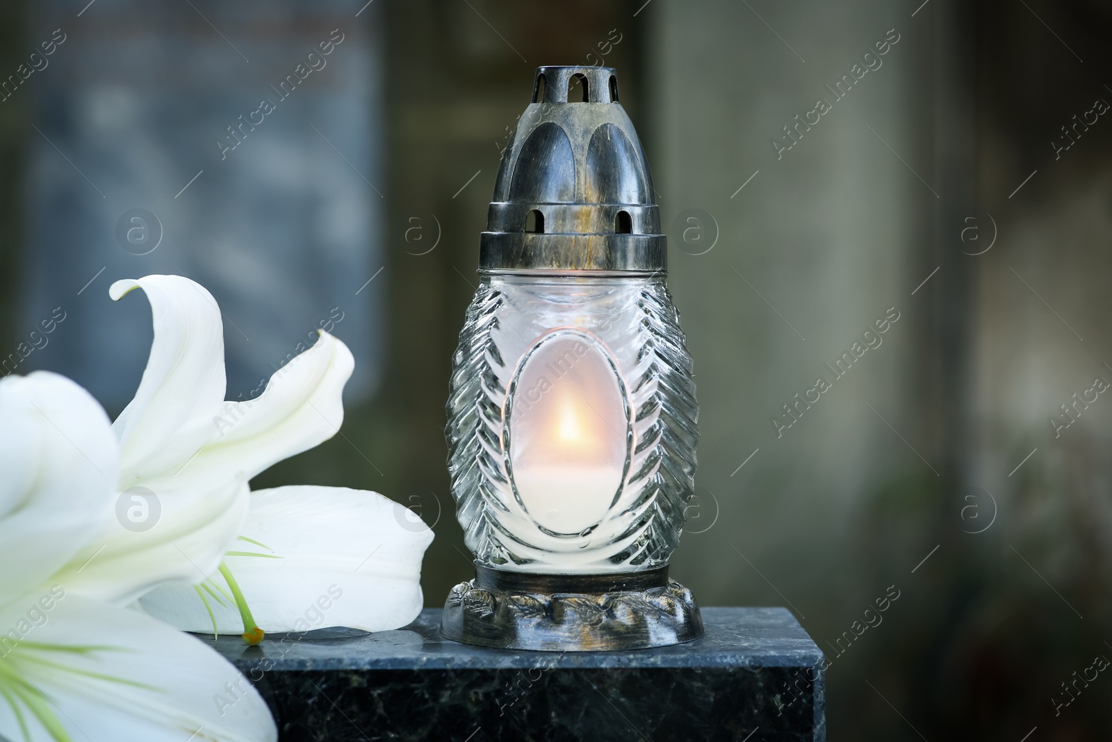 Photo of Lilies and grave lantern with burning candle on tombstone in cemetery, space for text