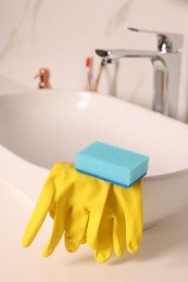 Photo of Sponge and rubber gloves on bathroom sink indoors