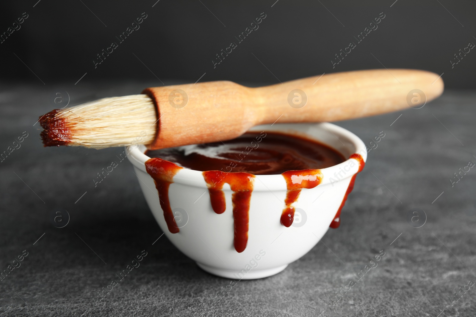 Photo of Bowl with barbecue sauce and brush on grey table