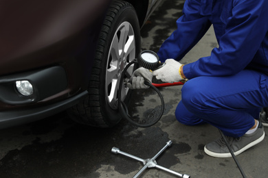 Worker checking tire pressure in car wheel at service station, closeup