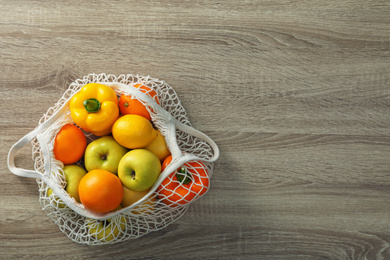 Net bag with vegetables and fruits on wooden table, top view. Space for text