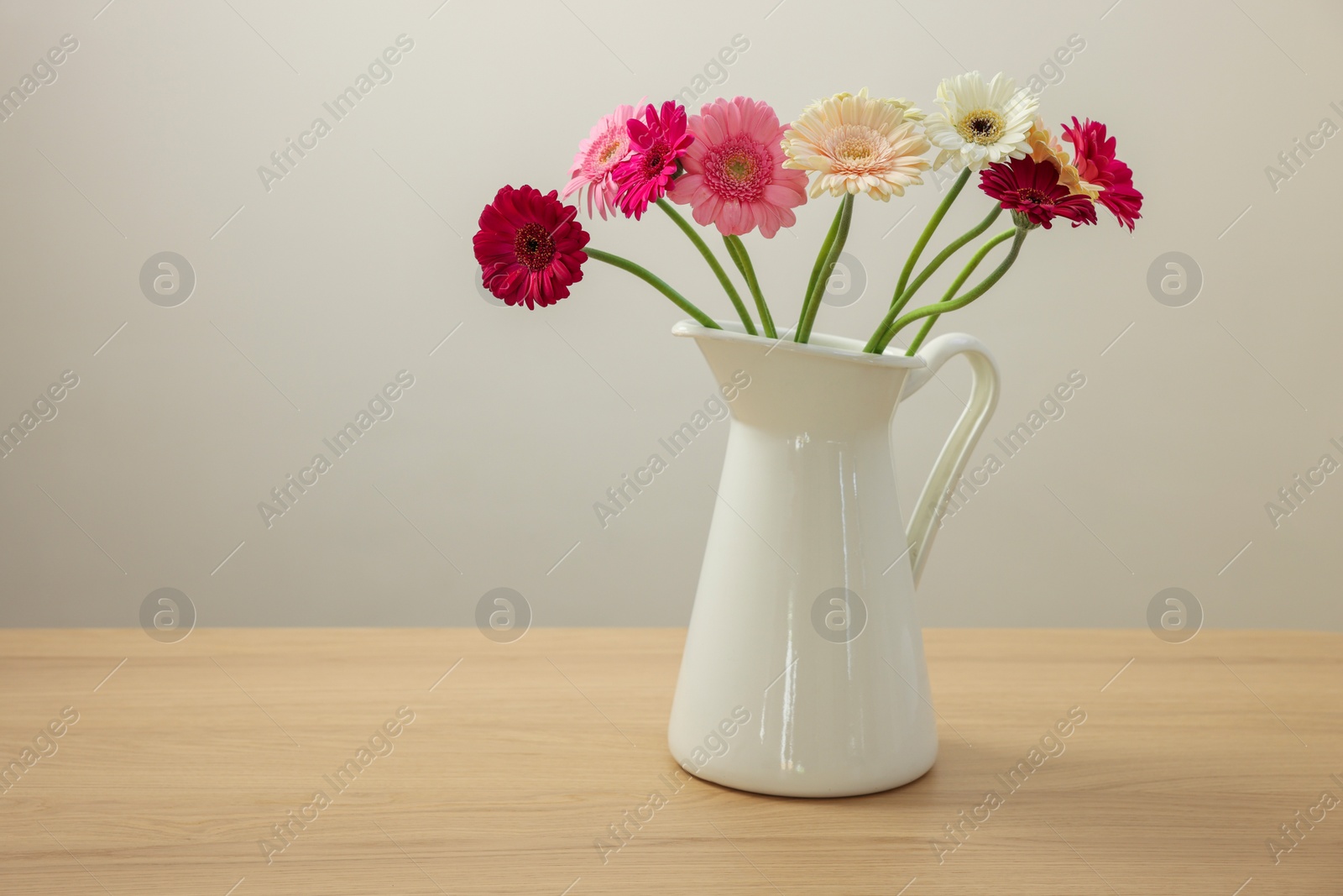 Photo of Jug with beautiful gerbera flowers on wooden table. Space for text