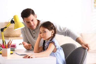 Father scolding his daughter while helping with homework at table indoors