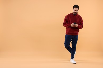 Photo of Happy young man using smartphone on beige background, space for text