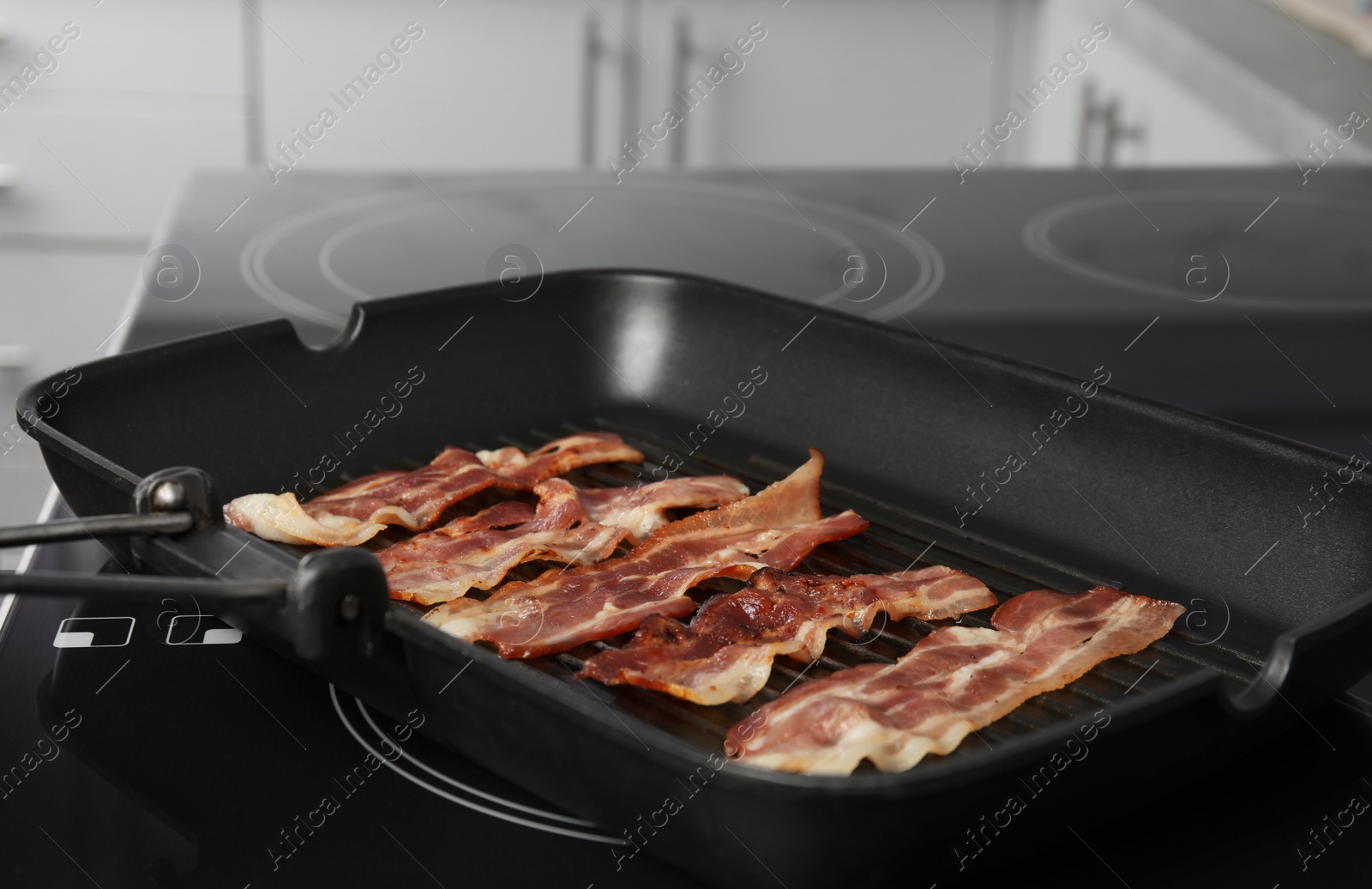 Photo of Slices of tasty fried bacon in grill pan indoors