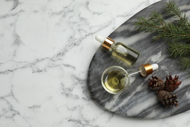Photo of Pine essential oil, cones and branch on white marble table, top view. Space for text