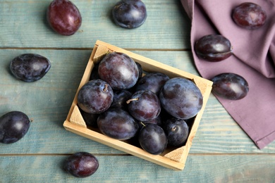 Delicious ripe plums in crate on blue wooden table, flat lay