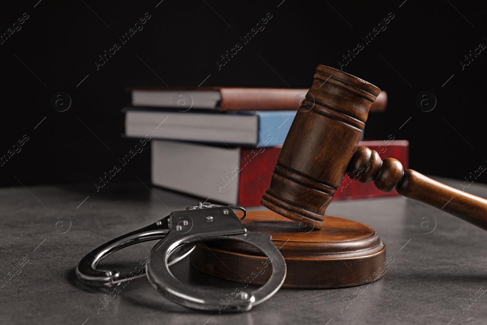 Photo of Judge's gavel, handcuffs and books on grey table against black background. Criminal law concept