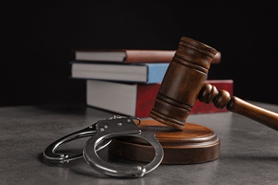 Photo of Judge's gavel, handcuffs and books on grey table against black background. Criminal law concept