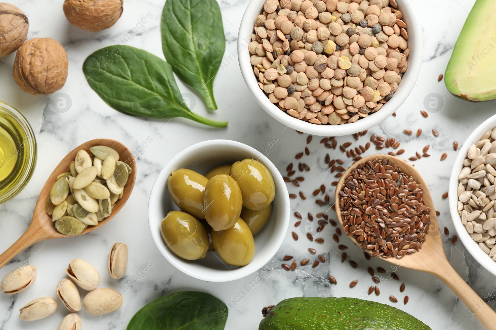 Photo of Different products and seeds high in healthy fats on white marble table, flat lay