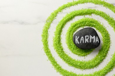 Photo of Stone with word Karma and circle made of light green sea salt on white marble table, top view . Space for text