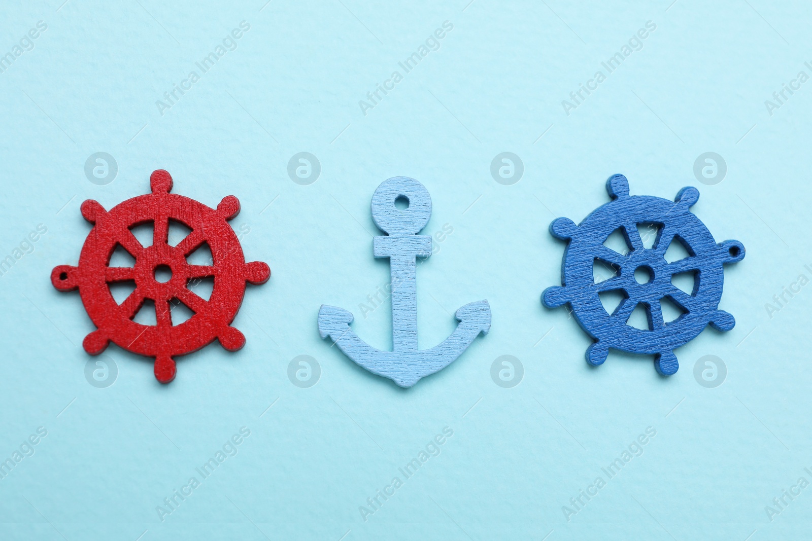 Photo of Anchor and ship wheel figures on pale blue background, flat lay