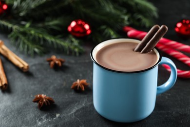 Photo of Delicious hot chocolate with cocoa sticks near Christmas decor on black table, closeup. Space for text
