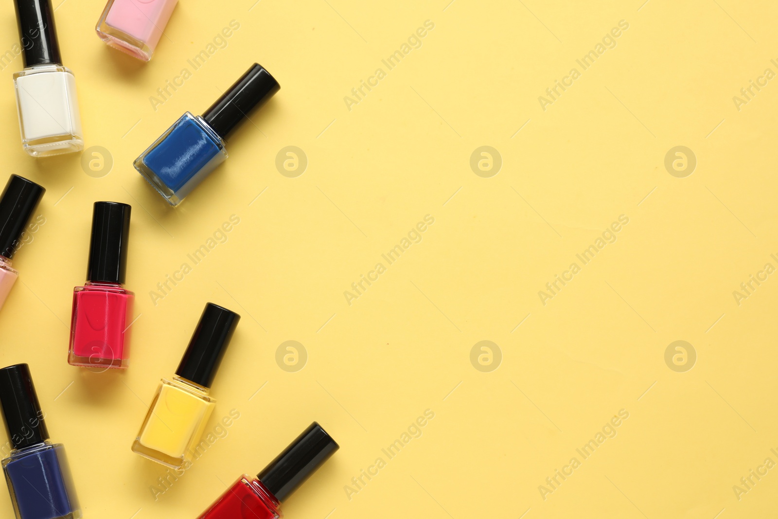 Photo of Bright nail polishes in bottles on yellow background, flat lay. Space for text