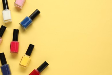 Bright nail polishes in bottles on yellow background, flat lay. Space for text