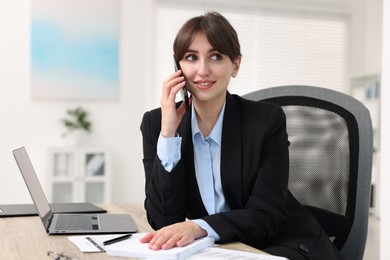 Smiling secretary talking by smartphone at table in office