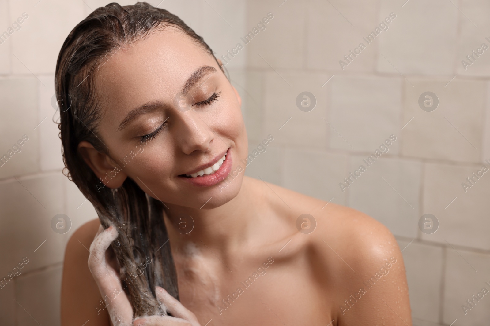 Photo of Happy woman washing hair while taking shower at home
