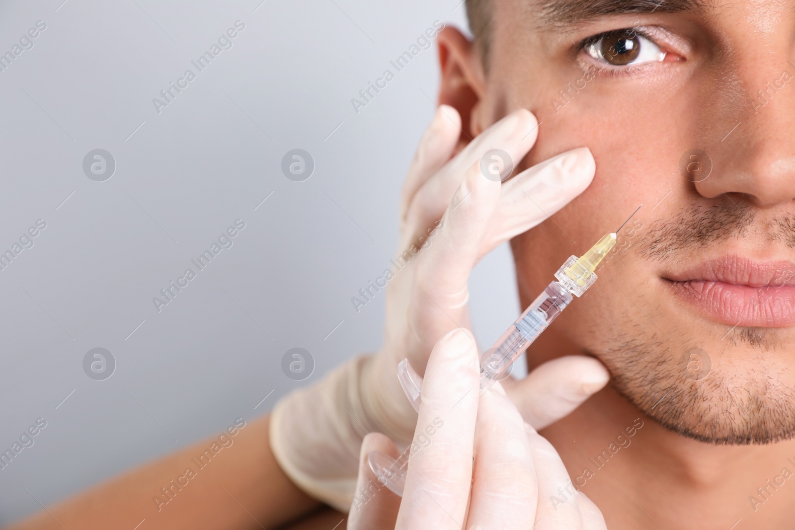 Photo of Man getting facial injection on grey background, closeup. Cosmetic surgery
