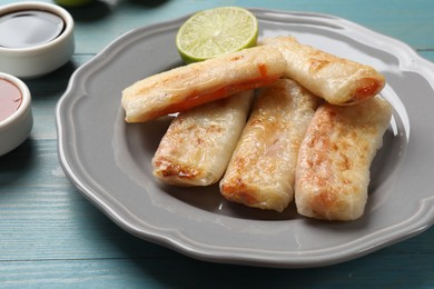 Delicious fried spring rolls served on light blue wooden table, closeup