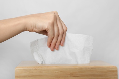 Photo of Woman taking paper tissue from holder on light background, closeup