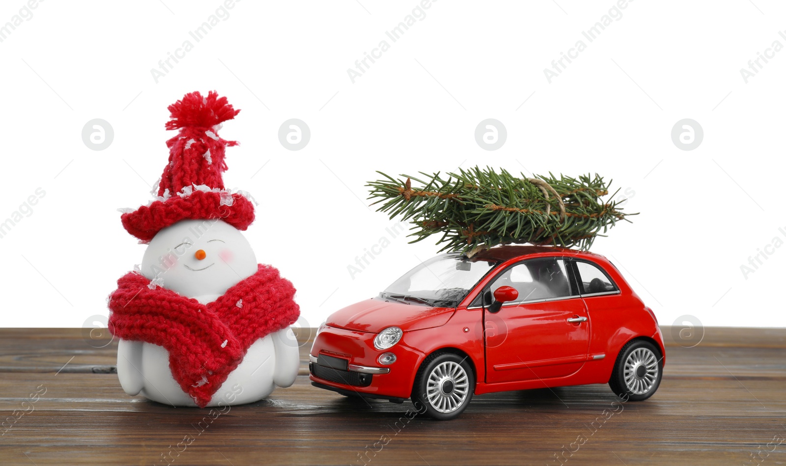 Photo of Cute decorative snowman, toy car and fir tree branches on wooden table against white background