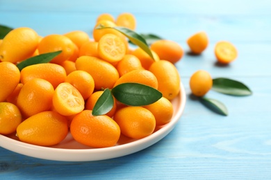 Photo of Fresh ripe kumquats in plate on light blue wooden table. Space for text