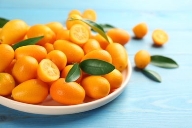 Fresh ripe kumquats in plate on light blue wooden table. Space for text