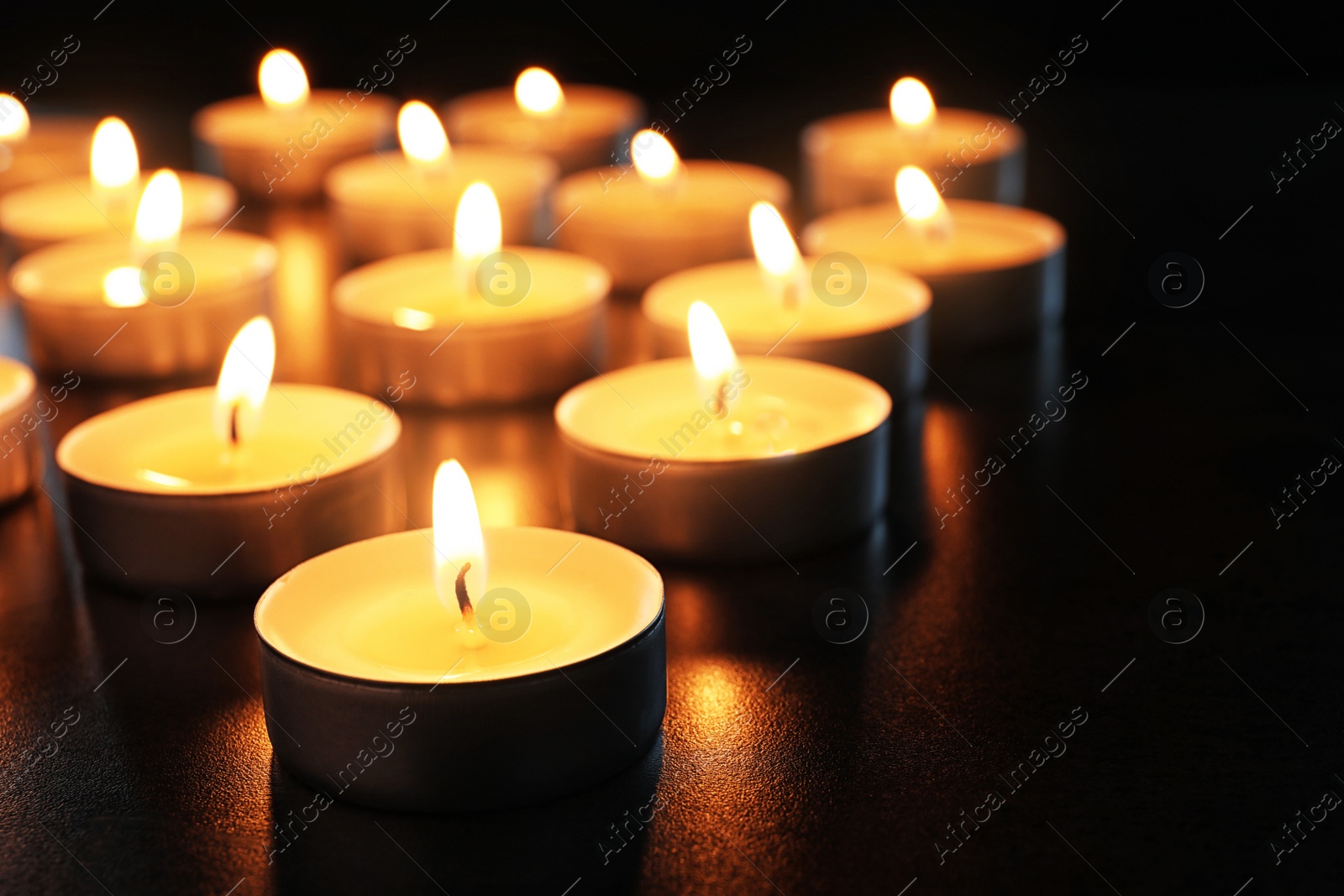 Photo of Wax candles burning on table in darkness, closeup