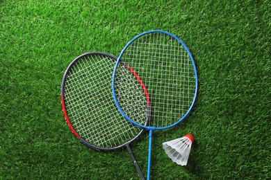 Photo of Two badminton rackets and shuttlecock on green grass, top view